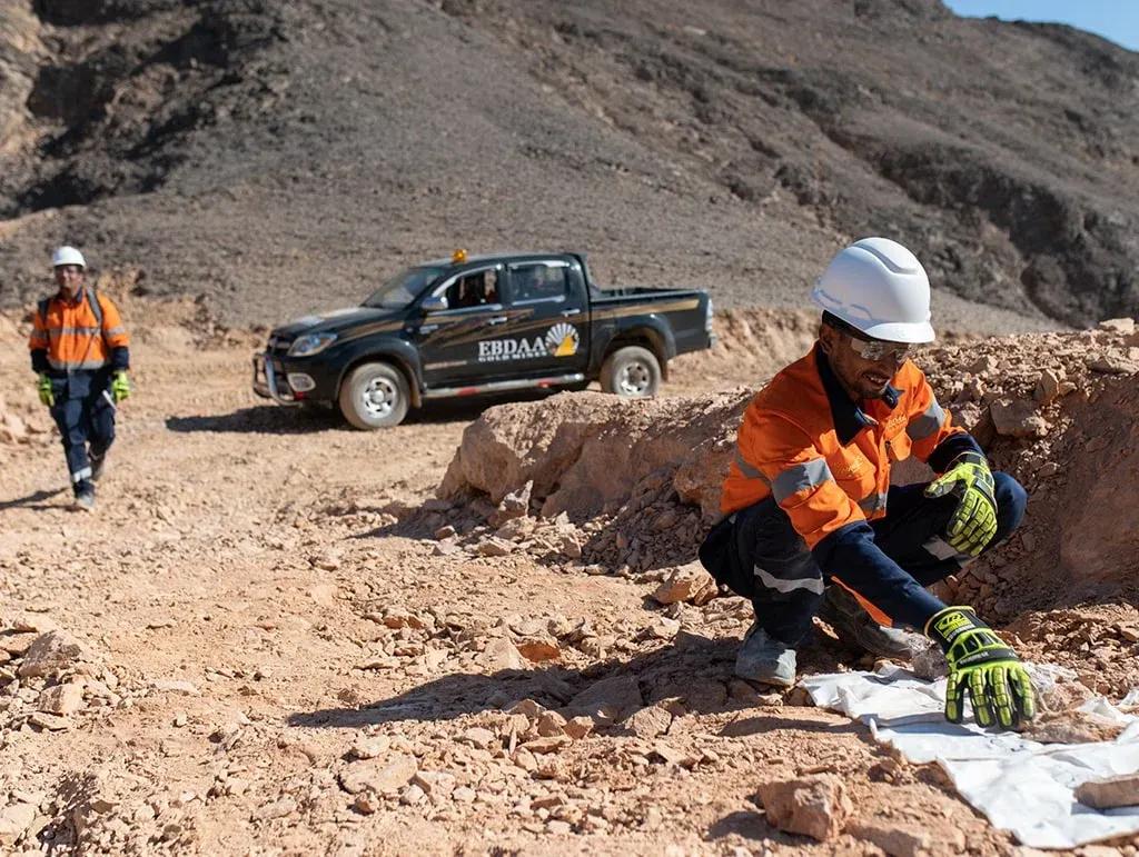 EBDAA geologist sampling rock at a surface outcrop beside a field truck